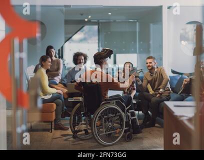Disabled businessman in a wheelchair at work in modern open space coworking office with team using virtual reality googles drone assistance simulation Stock Photo