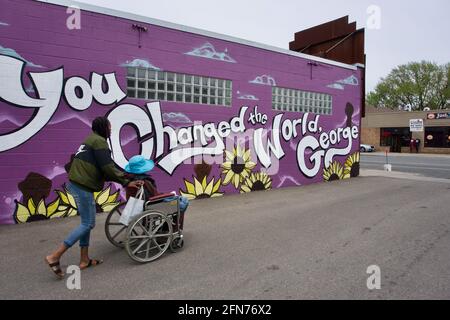 Woman pushing another in a wheelchair at George Floyd Square in front of a mural that says "You Changed The World, George". Minneapolis, MN, USA Stock Photo