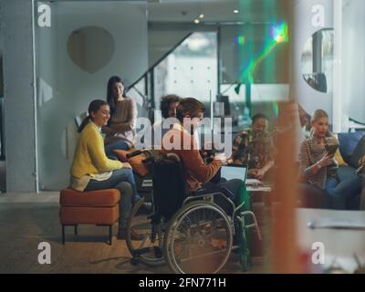 Disabled businessman in a wheelchair at work in modern open space coworking office with team using virtual reality googles drone assistance simulation Stock Photo