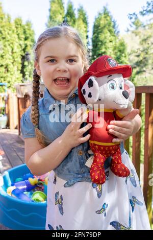Lynwood, Washington, USA.  Four year old girl having fun with her stuffed fireman dog.  (MR) Stock Photo
