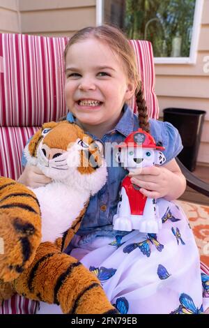 Lynwood, Washington, USA.  Four year old girl having fun with her stuffed fireman dog and tiger.  (MR) Stock Photo