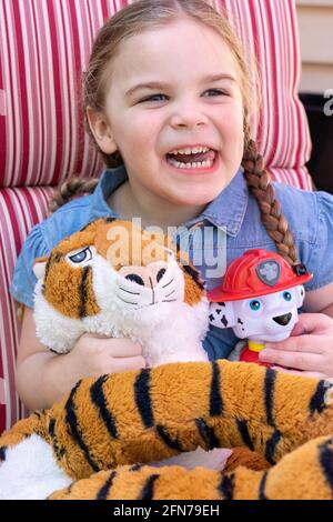 Lynwood, Washington, USA.  Four year old girl having fun with her stuffed fireman dog and tiger.  (MR) Stock Photo