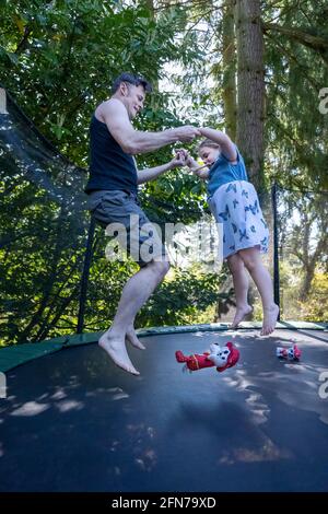 Lynwood, Washington, USA.  Four year old girl and her father bouncing on a trampoline in their backyard. Stock Photo