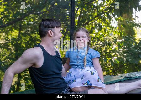 Lynwood, Washington, USA.  Father and four year old daughter taking a rest on their backyard trampoline after playtime. Stock Photo