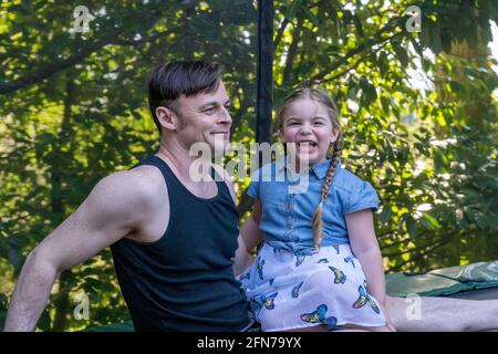 Lynwood, Washington, USA.  Father and four year old daughter taking a rest on their backyard trampoline after playtime. Stock Photo