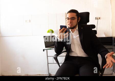 Hispanic young man in a black suit doing home office at his desk very angry about work Stock Photo