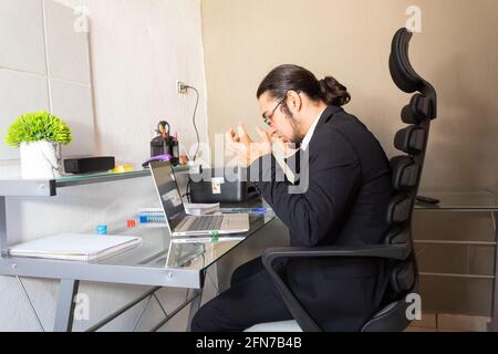 Hispanic young man in a black suit doing home office at his desk very angry about work Stock Photo