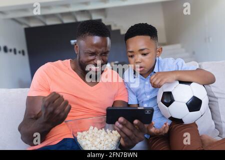 African american father and son sitting on sofa, using samrtphone Stock Photo
