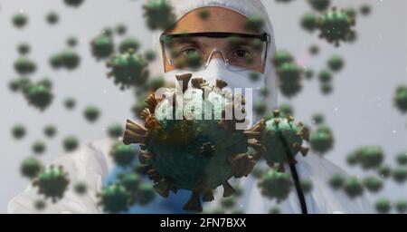 Composition of covid 19 cells floating over doctor in ppe suit and face mask Stock Photo