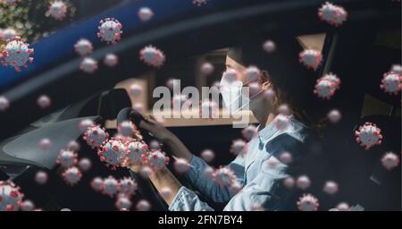 Composition of covid 19 cells floating over woman in car in face mask Stock Photo