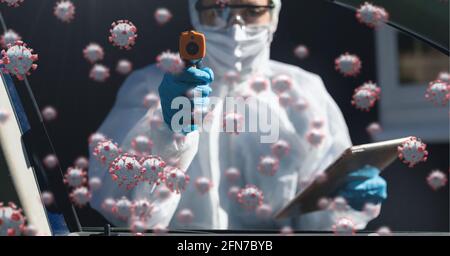Composition of covid 19 cells floating over doctor in ppe suit and face mask measuring temperature Stock Photo