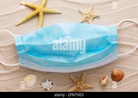 Medical mask and seashells on the sand, concept on the theme of wearing personal protective equipment on the beach. Stock Photo