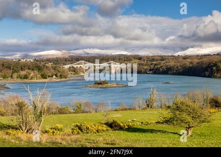 Evening on the Menai Strait and Suspension Bridge, Anglesey, with the snow covered mountains of Snowdonia in the distance. Stock Photo