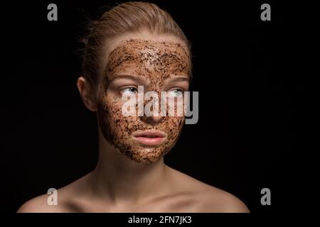 Skin scrub Coffee grounds mask on the face of a beautiful young woman Organic natural cosmetology dark studio background Isolate Stock Photo