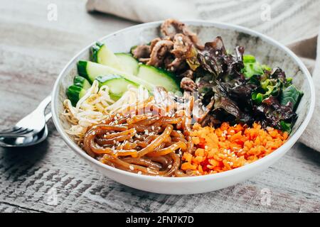 Asian buddha bowl on wooden table background. Delicious balanced food concept Grilled beef, carrot, cucumber, sprouted mung bean, topinambour noodles, Stock Photo