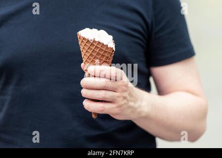 A brutal man dressed in black t-shirt holding an Ice cream in his hand at a city park Stock Photo