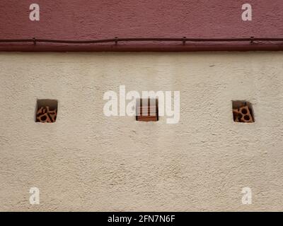 Reddish-yellowish wall with a thick wire and several square holes with bricks in them Stock Photo