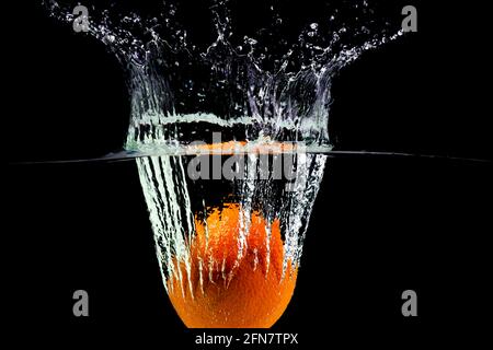 one orange fell into the water with splashes and bubbles Stock Photo