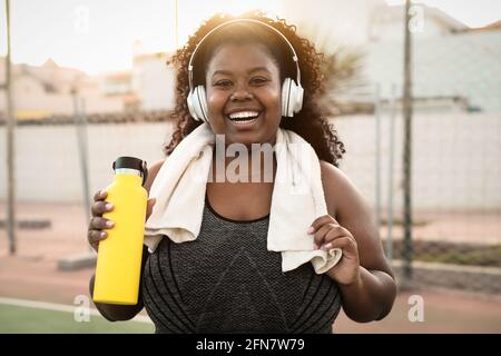 Sport curvy black woman listening music with headphones - Focus on