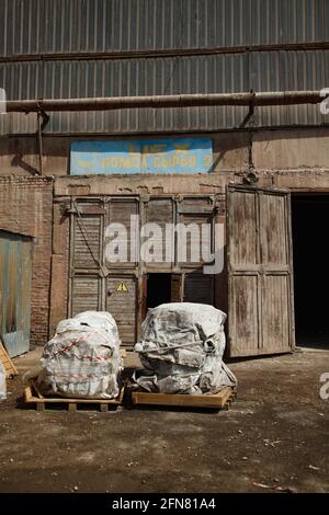 Temirtau,Kazakhstan:Outdated Soviet cement plant building.Old wooden doors (gates).Title:'Raw Mill Workshop'. Equipment on pallets wrapped in cloth. Stock Photo
