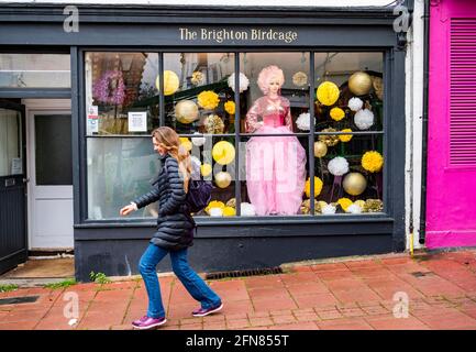 Brighton UK 15th May 2021 - A young lady dashes down the street past the Brighton Birdcage shop in Brighton as wet weather sweeps across most parts of Britain today : Credit Simon Dack / Alamy Live News Stock Photo