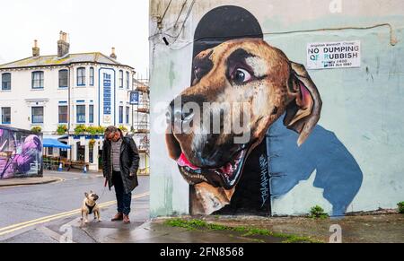 Brighton UK 15th May 2021 - It's a damp morning for this dog walker as his hound looks slightly anxious at a large mural in Brighton as wet weather sweeps across most parts of Britain today : Credit Simon Dack / Alamy Live News Stock Photo