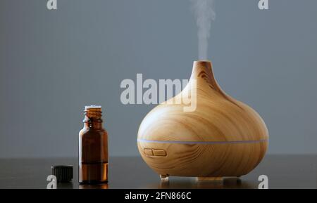Essential oil bottle with an electric ultrasonic humidifier that emits atomized water droplets on a dark background. The device is round in shape with Stock Photo