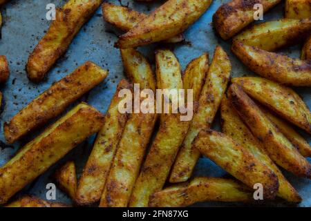 Homemade spicy baked potatoes on a baking sheet and on greaseproof paper. selective focus sliced potato. Stock Photo