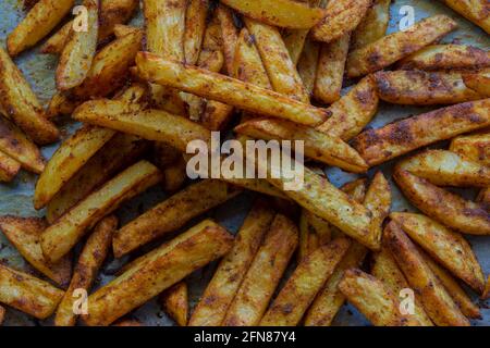 Homemade spicy baked potatoes on a baking sheet and on greaseproof paper. selective focus sliced potato. Stock Photo