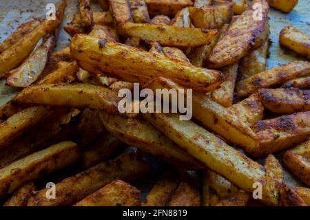 Homemade spicy baked potatoes on a baking sheet and on greaseproof paper. selective focus sliced potato. Stock Photo