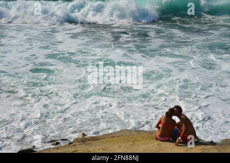 Seascape with a young couple sitting on a rock off the shore of Oceanside Beach in San Diego, California USA.