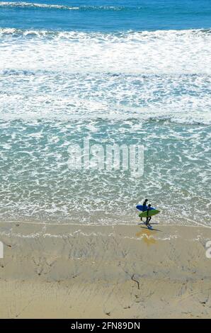 Seascape with panoramic view of two surfers walking with their surfboards on the shoreline of Carlsbad State Beach in San Diego,  California USA. Stock Photo