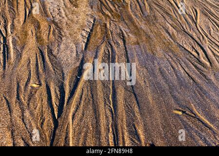 Close up of water flowing through sand ripples or tide lines under a winter sun Stock Photo