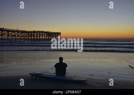 Sunset seascape with a surfer on the shoreline of Pacific Beach overlooking Crystal Pier in San Diego, Southern California USA. Stock Photo