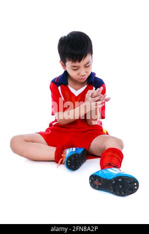 Sports injure. Youth asian soccer player in red uniform injured at hand. Isolated on white background. Studio shot. Full body. Stock Photo