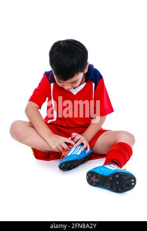 Sports injure. Youth asian soccer player in red uniform injured at ankle joint. Isolated on white background. Studio shot. Full body. Stock Photo