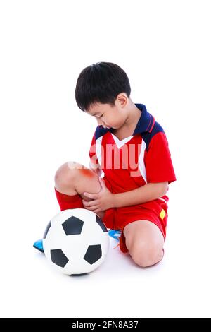 Sports injure. Youth asian soccer player with football in red uniform injured at his leg. Isolated on white background. Studio shot. Full body. Stock Photo