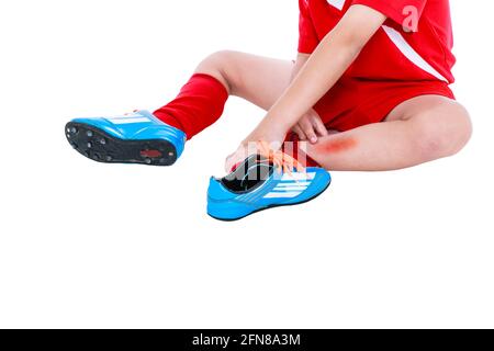 Sports injure. Youth asian soccer player in red uniform injured at leg. Isolated on white background with copyspace. Studio shot. Stock Photo