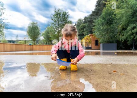 little girl playing with paper boats in puddle Stock Photo