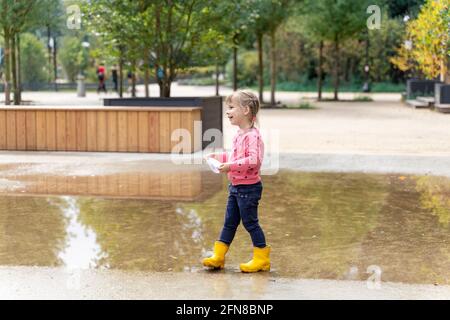 little girl playing with paper boats in puddle Stock Photo