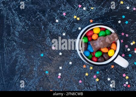 chocolate bunny on multi-colored chocolates in the form of eggs in a white mug on a black background. top view Stock Photo