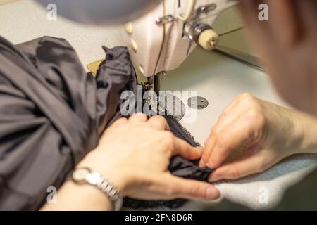 woman sews from dark fabric on a sewing machine. Stock Photo