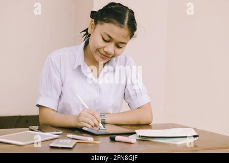Asian Thai cute girl teen student school uniform happy smile using Tablet PC for homework and E-Learning self isolated education happy smile concept Stock Photo