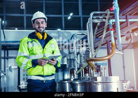 Happy engineer male worker working in factory using tablet computer to check boiler water pipe in factory, portrait smile. Stock Photo