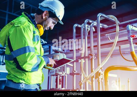 Factory worker engineer working in factory using tablet computer to check maintenance boiler water pipe in factory. Stock Photo