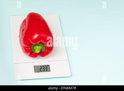 The concept of diet, proper nutrition, healthy eating. Fresh red bell peppers on kitchen scales isolated on blue background, copy space, close-up Stock Photo