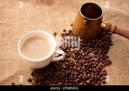 Cup of coffee and cezve with coffee beans on rustic rag. Vintage turk with roasted beans Stock Photo