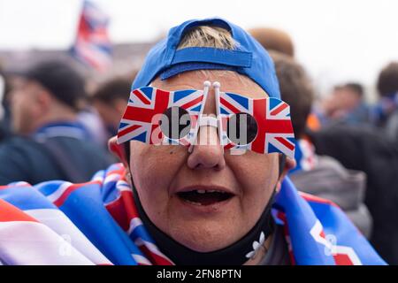 Glasgow, Scotland, UK. 15 May 2021. Thousands of supporters and fans of Rangers football club descend on Ibrox Park in Glasgow to celebrate winning the Scottish Premiership championship for the 55th time and the first time for 10 years. Smoke bombs and fireworks are being let off by fans tightly controlled by police away from the stadium entrances. Pic; Fans celebrate after full time at the gates of Ibriox. Iain Masterton/Alamy Live News Stock Photo