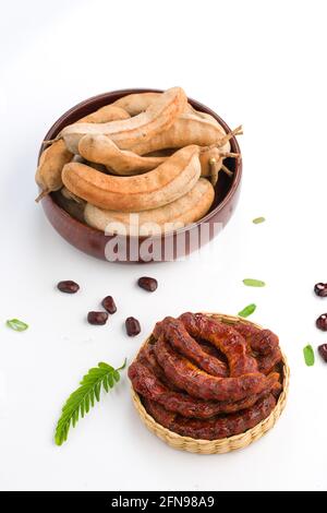 Tamarind  bean like pods filled with seeds surrounded by a fibrous pulp arranged in background with peeled tamarind filled in a basket,placed on white Stock Photo