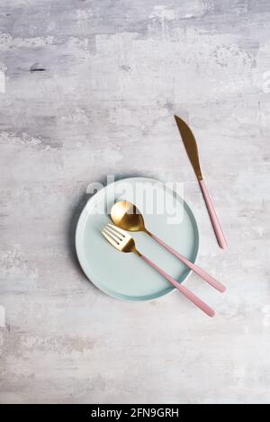 blue empty plates with gold fork, spoon and knife on a grey stone background, flat lay Stock Photo